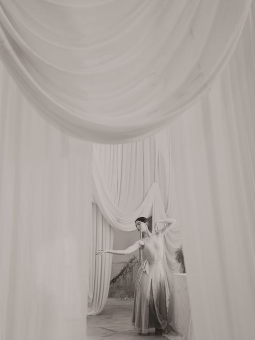 Free Elegant black and white photograph of a woman in a gown amidst flowing drapes. Stock Photo
