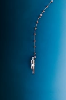 An aerial shot of an industrial pier extending into deep blue water, creating a conceptual abstract composition.