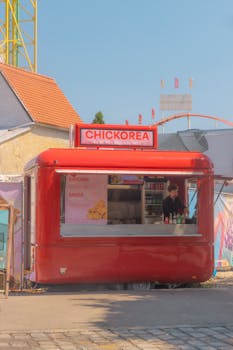 A vibrant red food truck named CHICKOREA serves chicken dishes at an outdoor setting with a sunny sky.