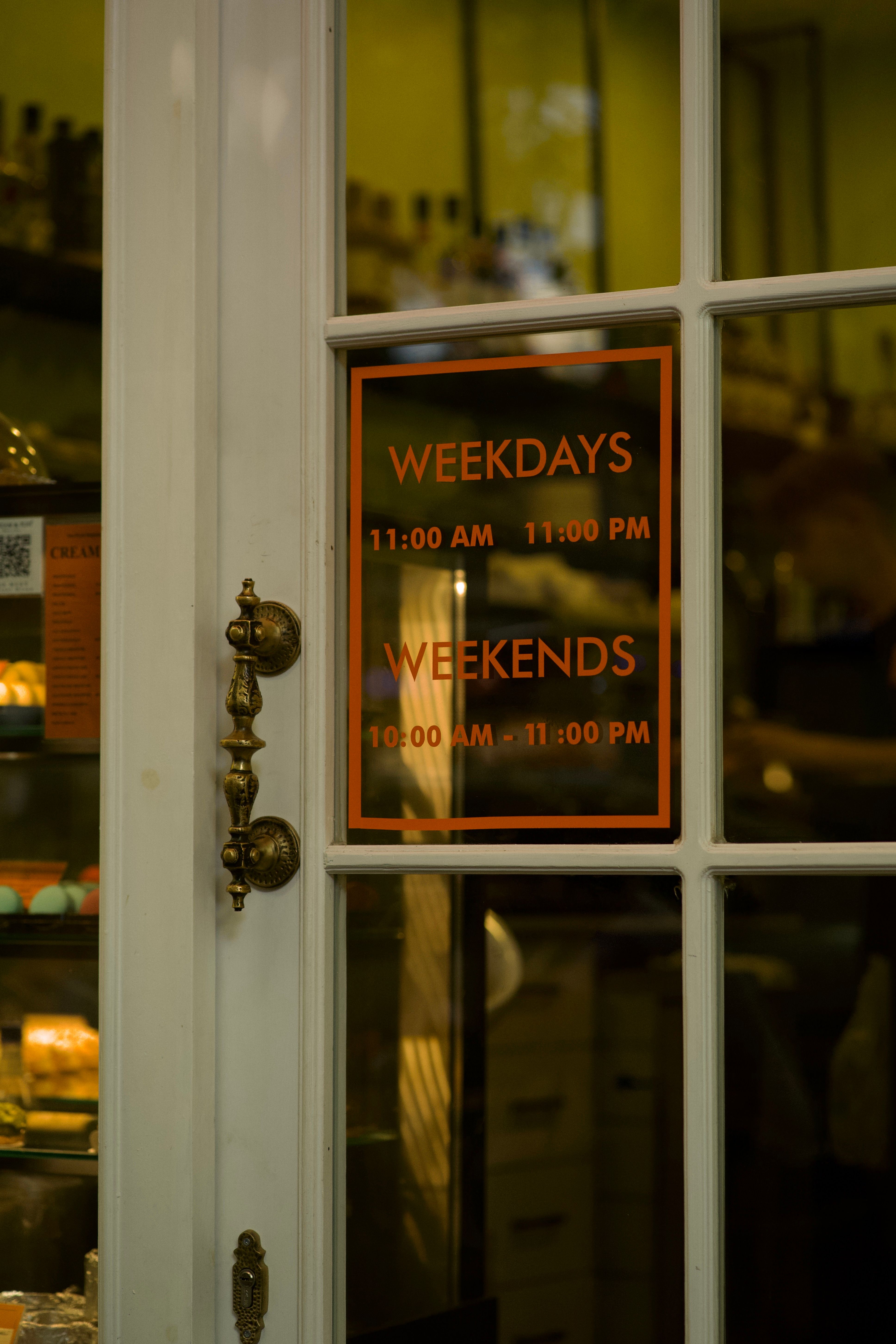 A storefront door with a vintage handle and business hours sign visible.