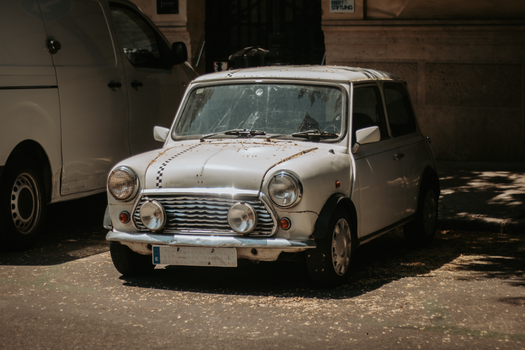 Classic Mini Cooper car parked on a city street in Madrid, Spain, bathed in sunlight.