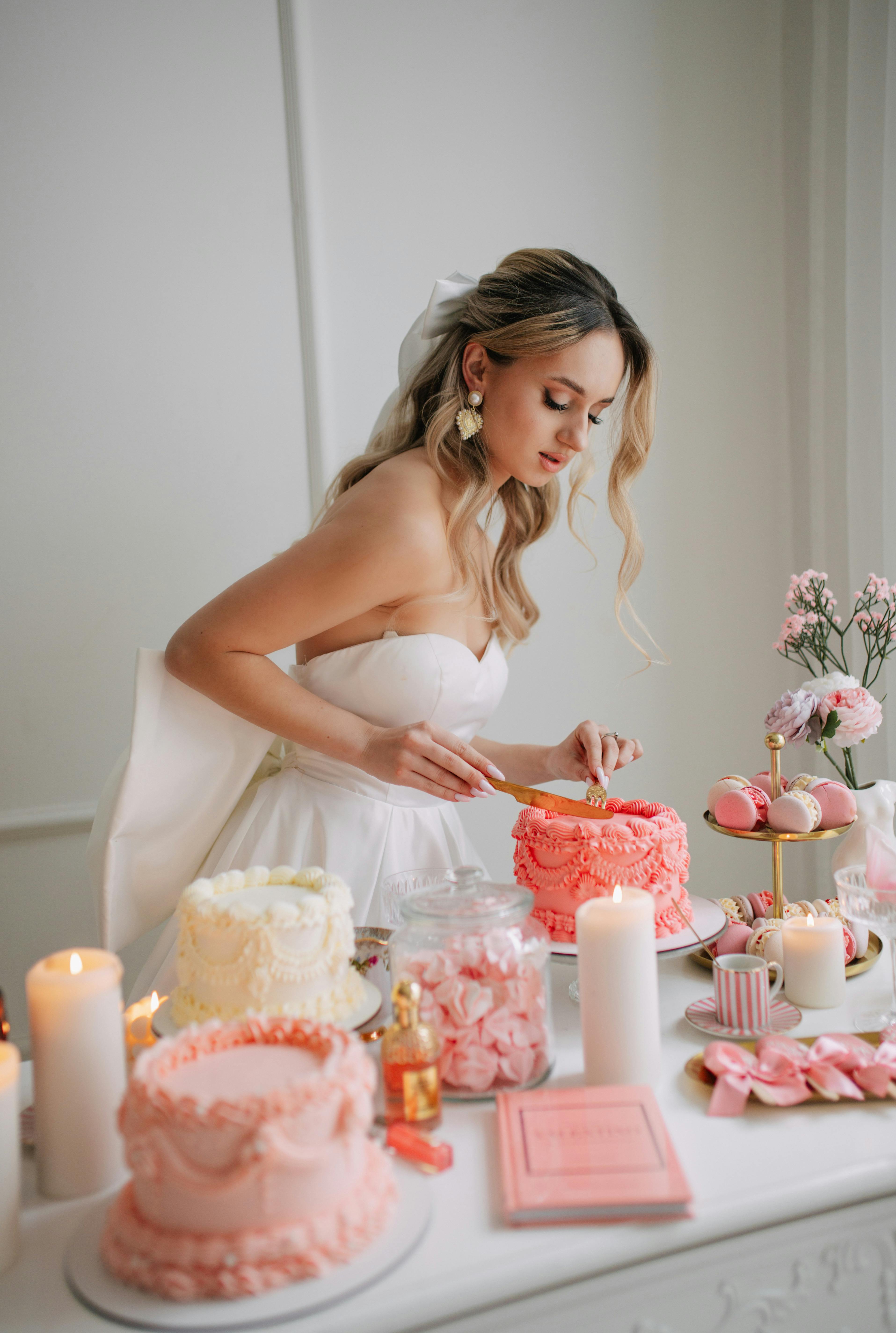 Bride elegantly decorates wedding cake in romantic, luxury setting with pink hues.