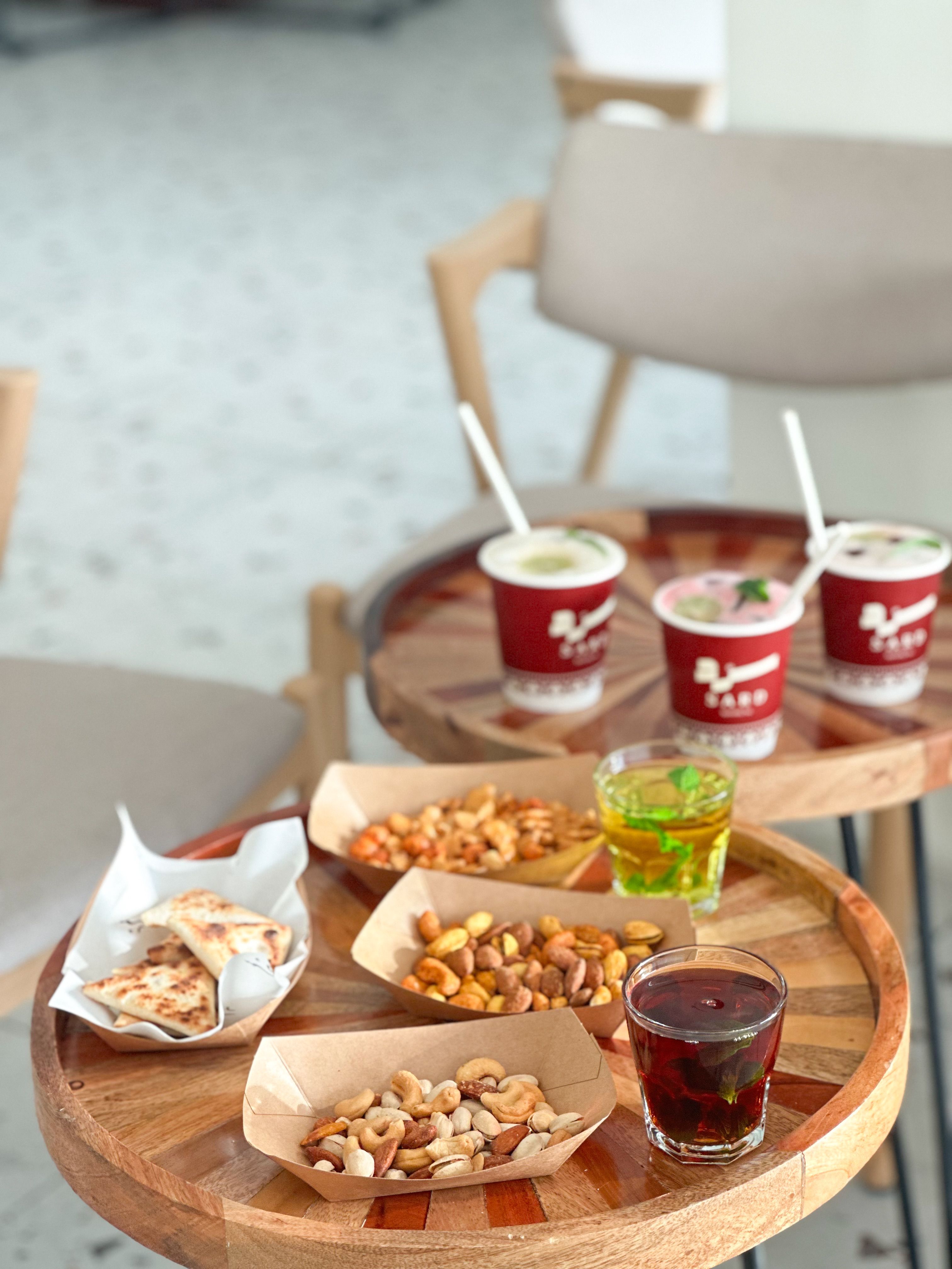 Assorted nuts, snacks, and drinks on rustic wooden tables in a cafe setting.