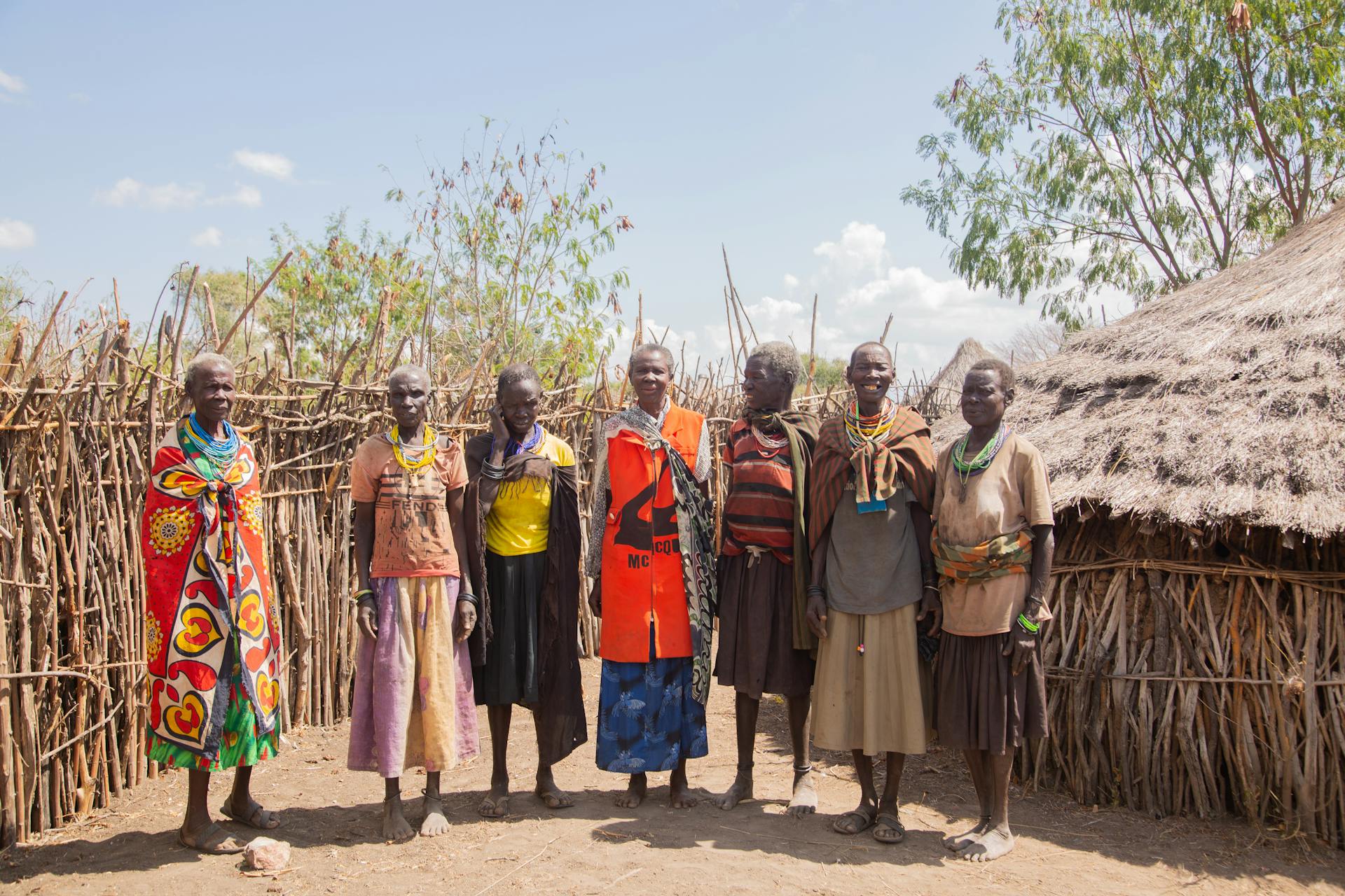 A group of Masai people standing together in a rural village, showcasing traditional clothing and huts.