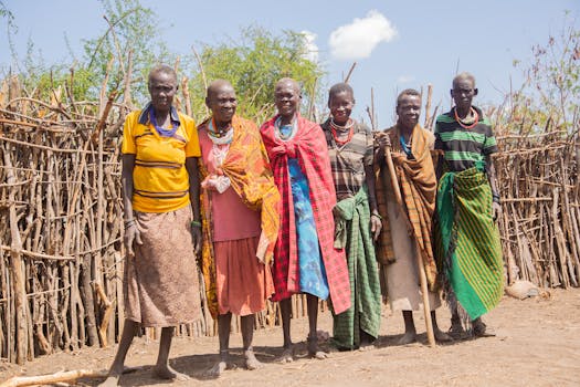 A group portrait of six adults in traditional tribal attire outdoors.