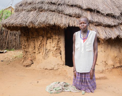 Free An adult tribal woman standing outside a traditional thatched-roof hut. Stock Photo