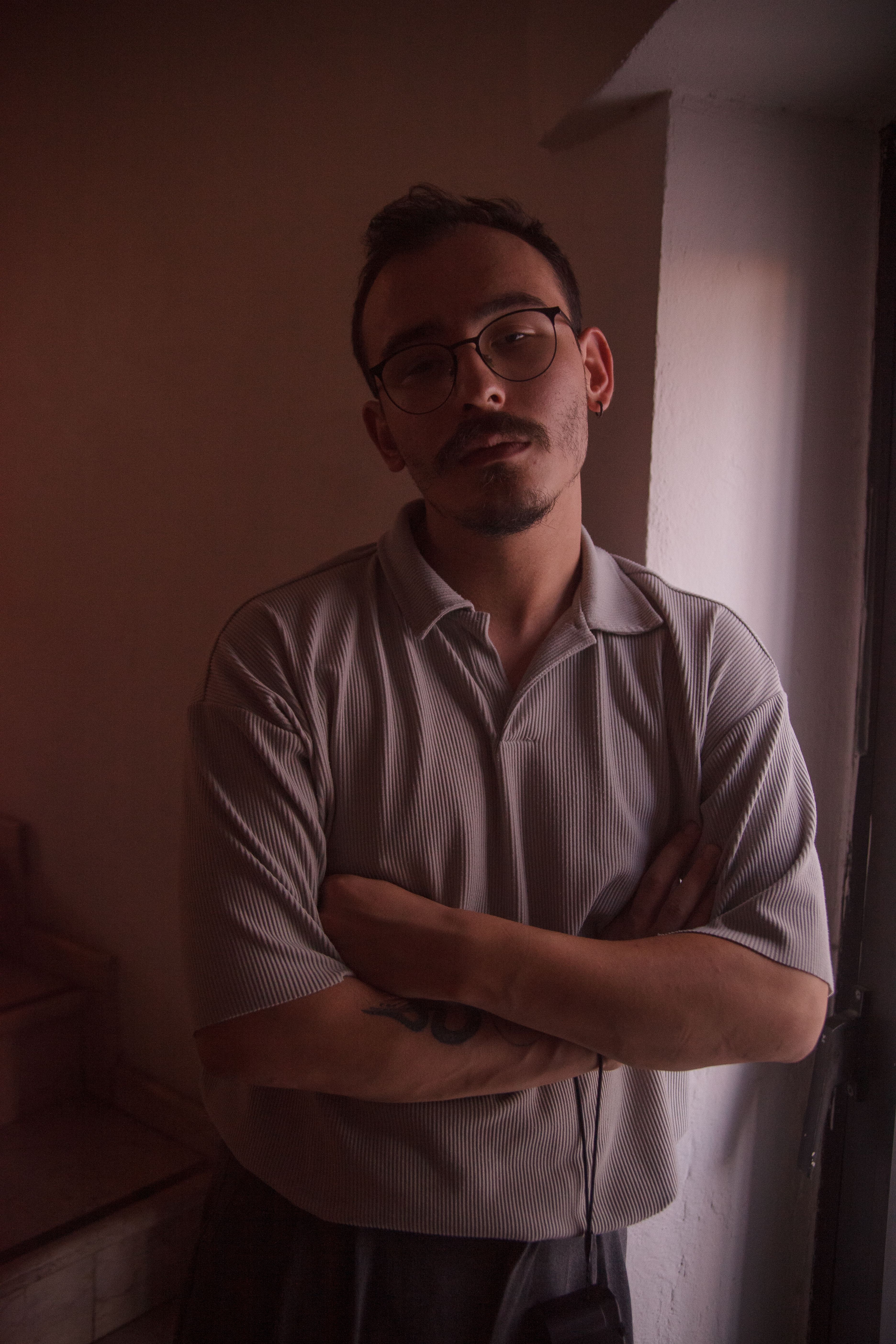 A thoughtful young man with glasses poses by the light indoors.