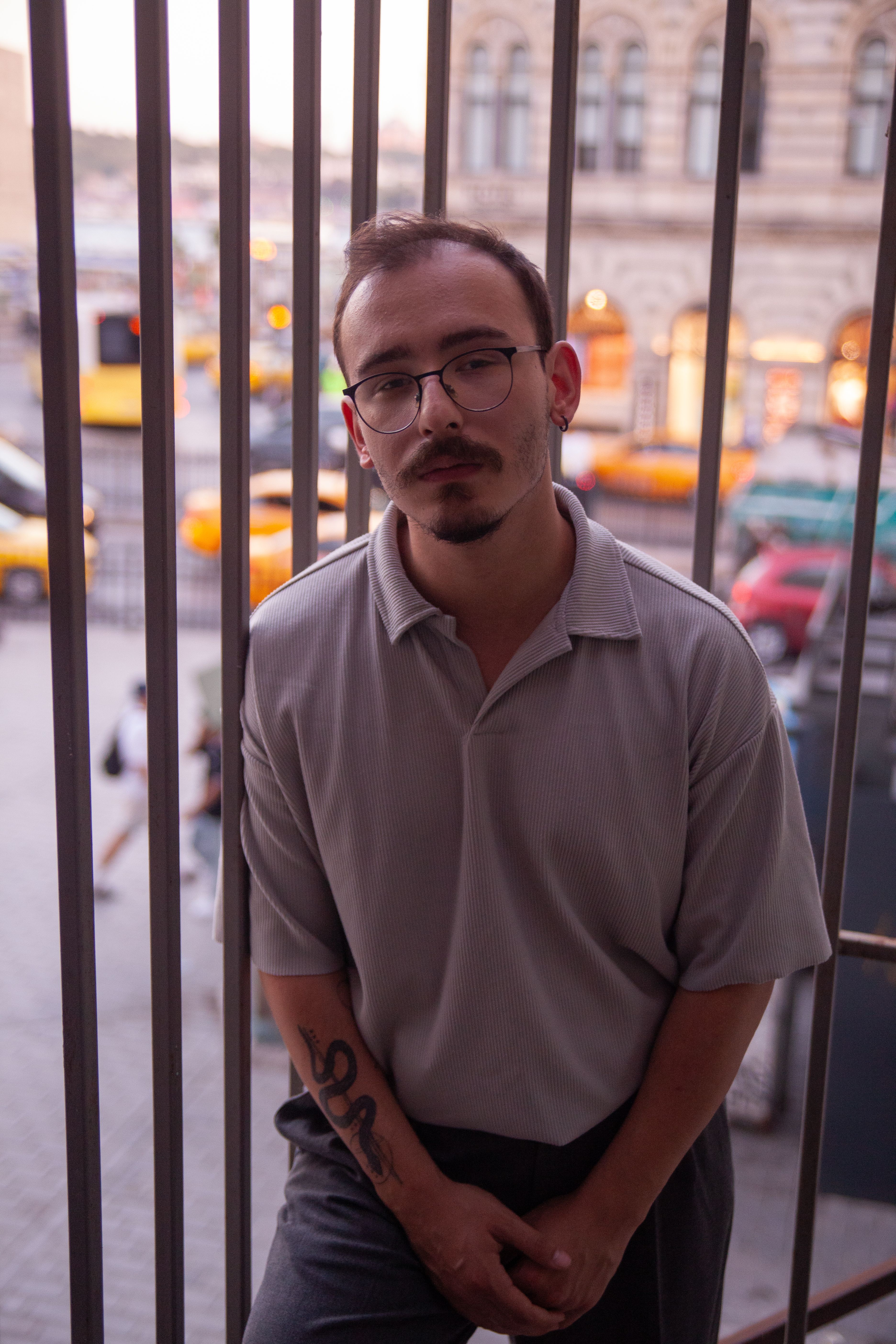 A contemplative man with eyeglasses stands pensively in an urban cityscape.