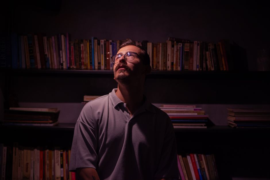Portrait of a man with eyeglasses in a moody library setting, surrounded by books.