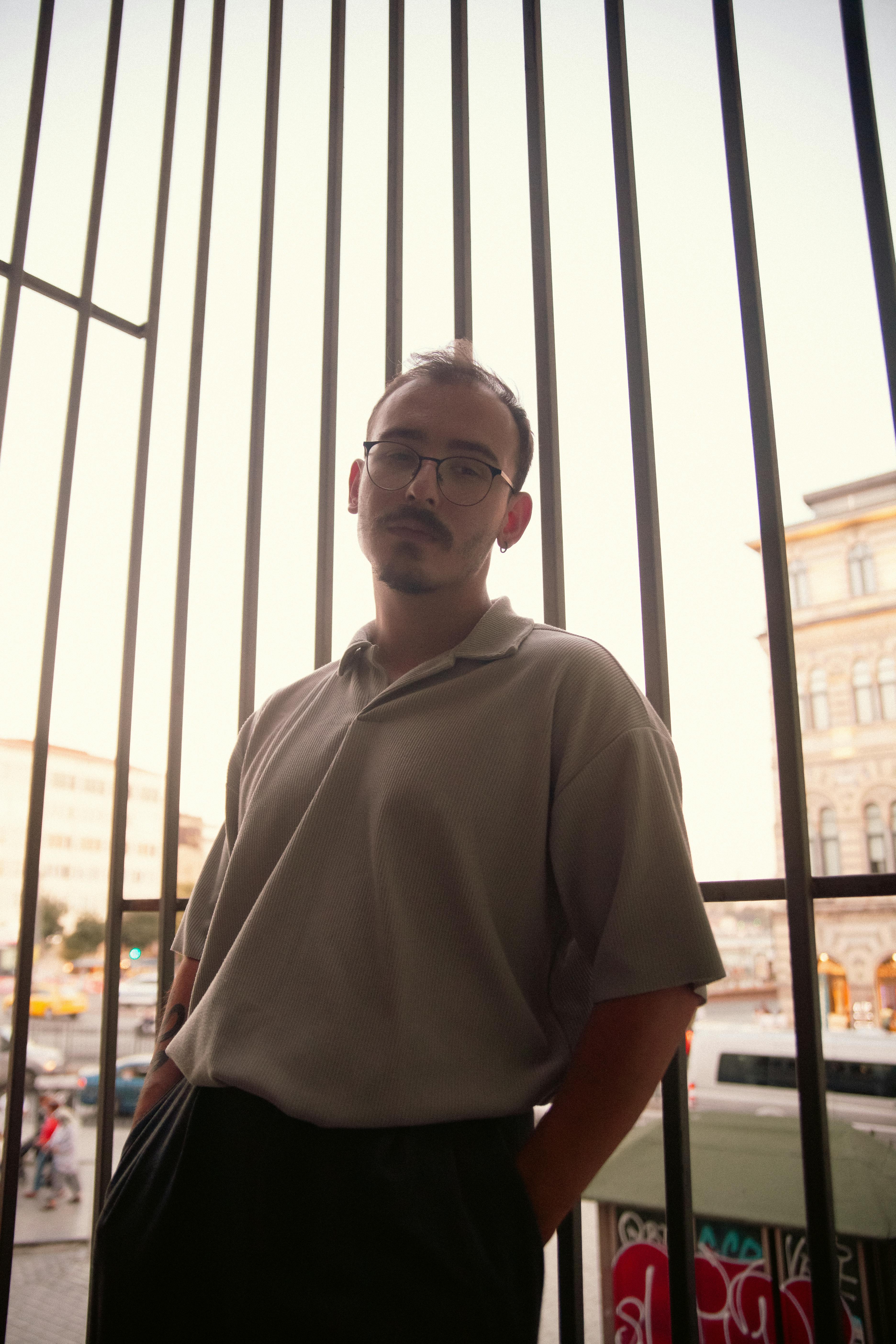 Portrait of a man wearing glasses standing against a city backdrop during the day.