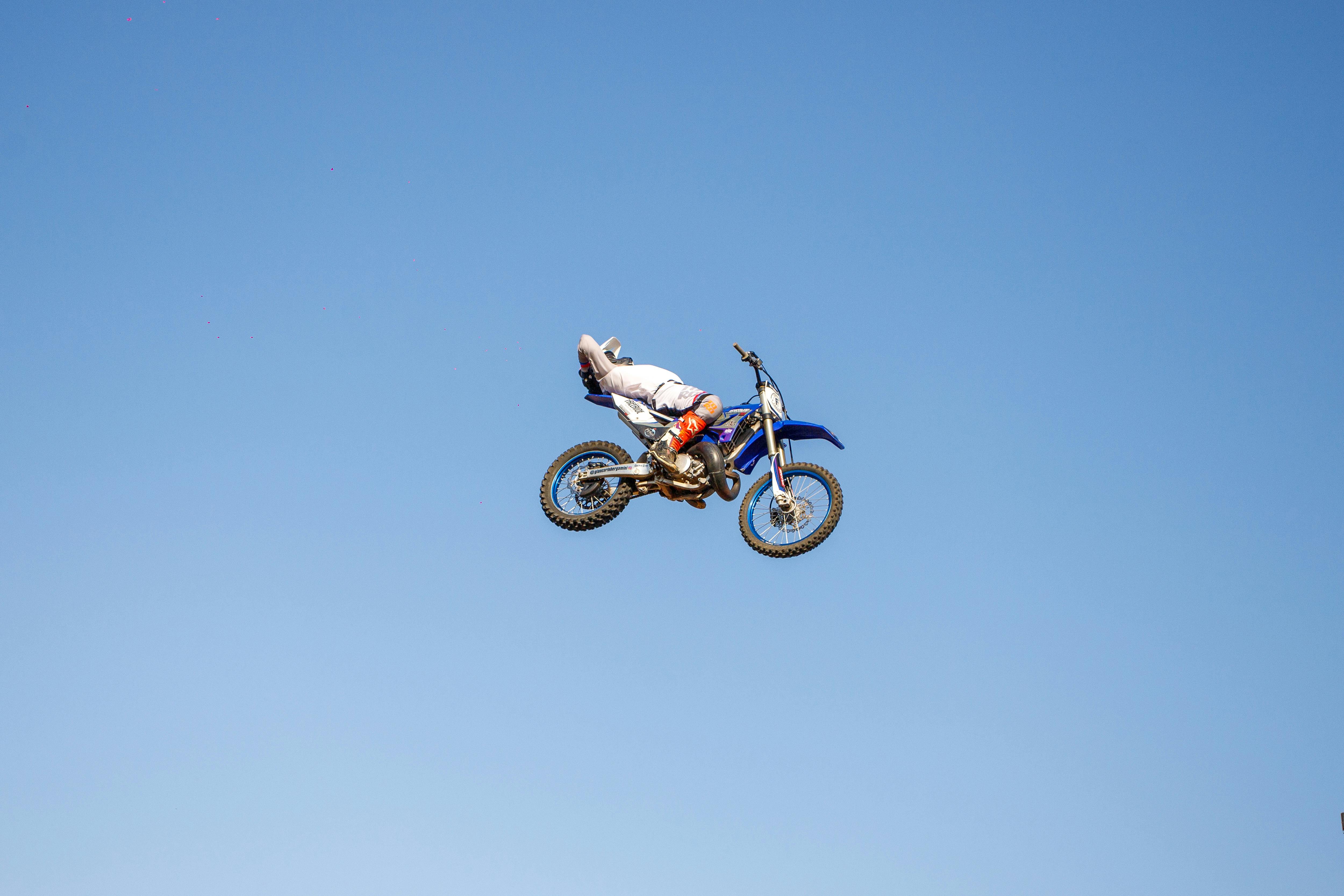 A motocross rider performs a daring stunt high in the blue sky, showcasing extreme sports skill.