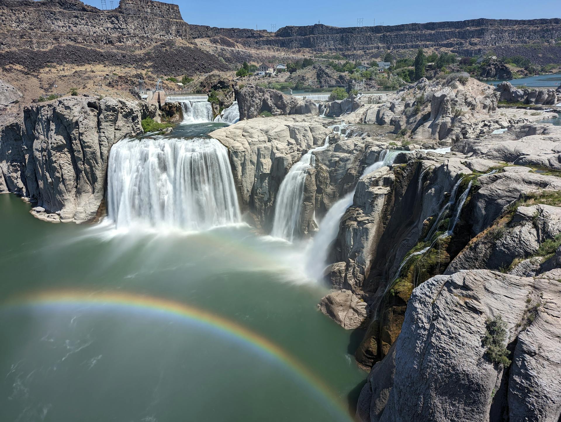 A rainbow appears over a waterfall in the middle of a river