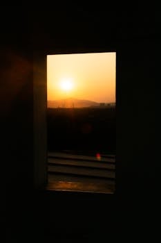 透过窗户，我看到了日落的剪影，捕捉到远处山脉上的金色光芒