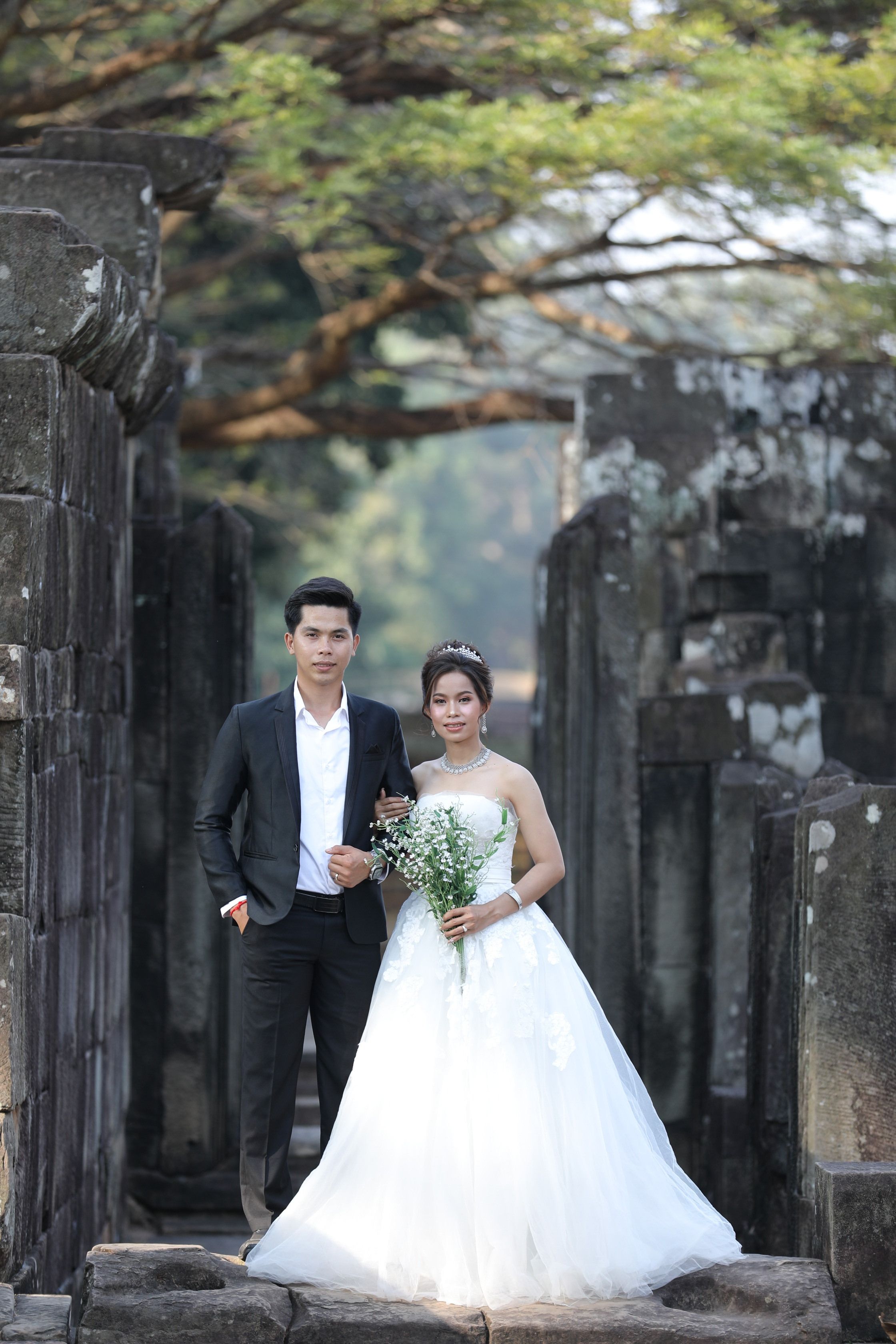 A bride and groom standing in front of a stone archway · Free Stock Photo