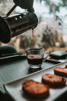 玻璃杯里倒入了芳香的咖啡，旁边的托盘上放着一盘脆饼