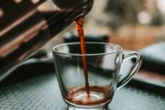 Close-up shot of coffee being poured from a French press into a glass cup with bokeh background.
