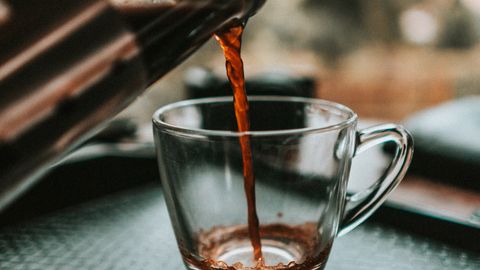 Close-up shot of coffee being poured from a French press into a glass cup with bokeh background.