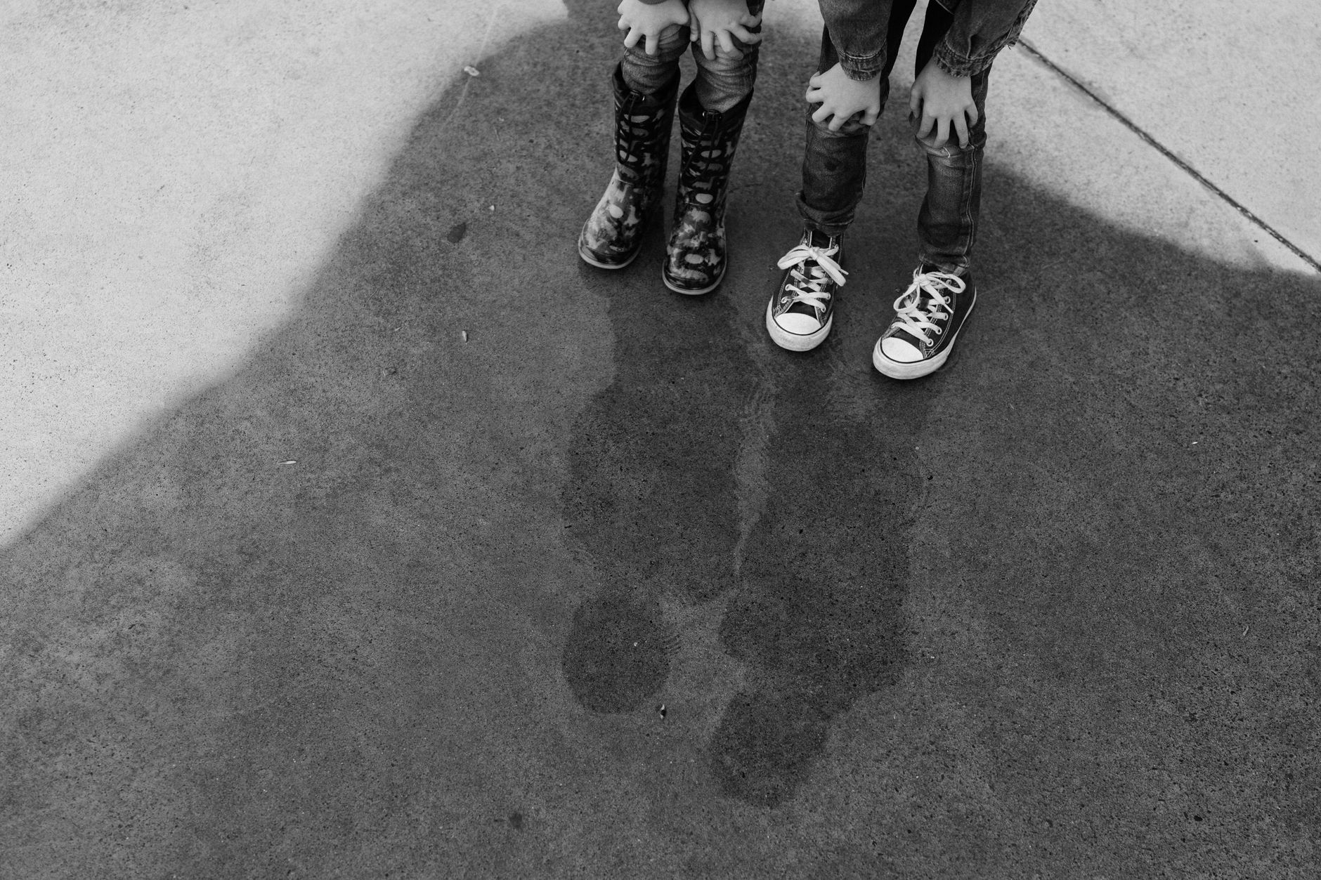 濡れた地面に映る二人の子どもの靴の白黒写真