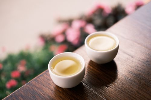 Free Two white tea cups on a wooden table with blurred flowers in the background. Stock Photo