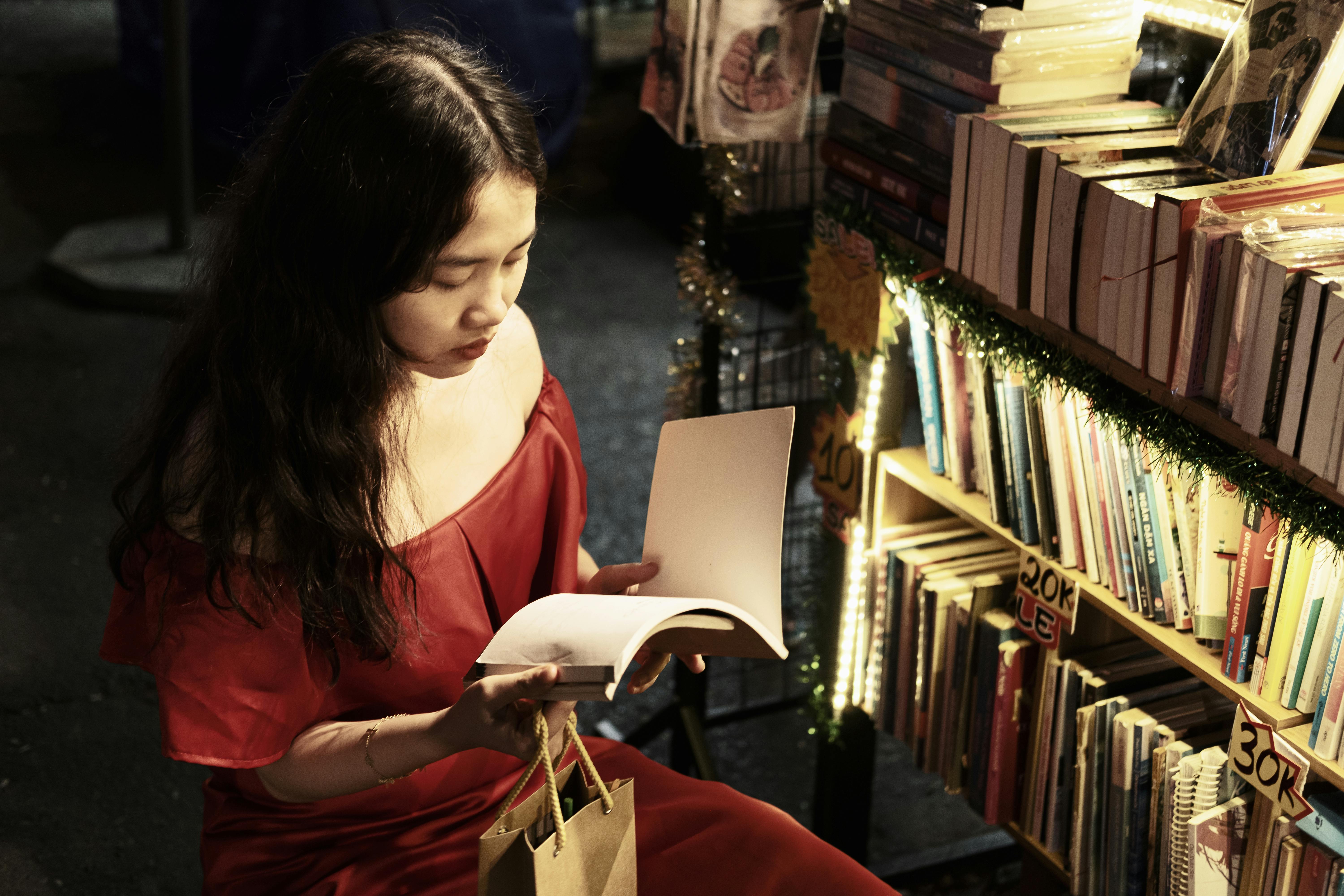 Woman reading a book at a dimly lit night market bookstall