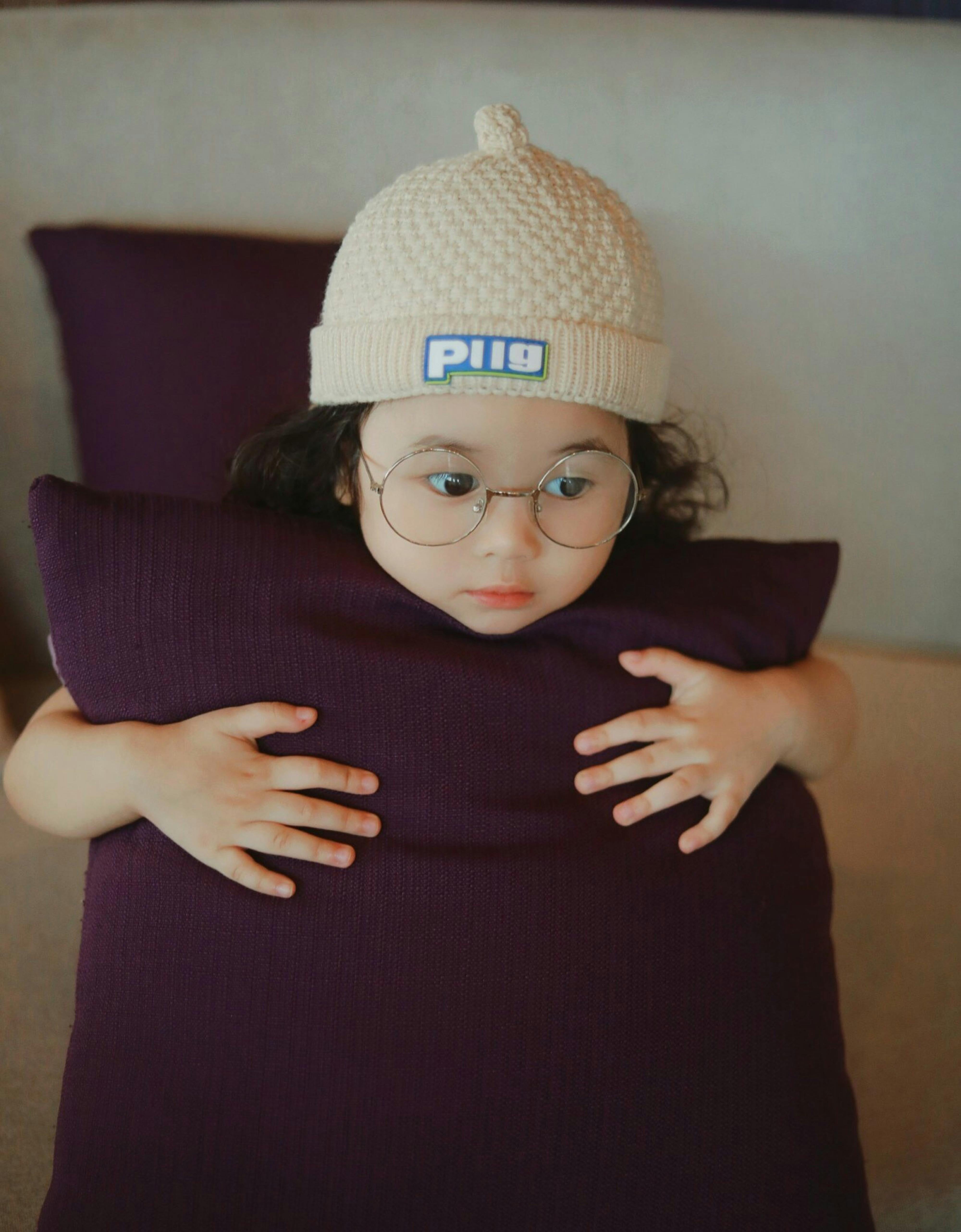 a little girl wearing glasses and a beanie on top of a pillow