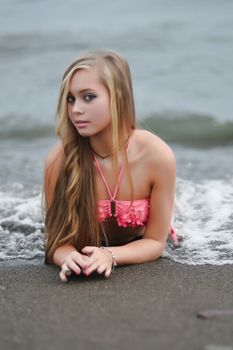 Young woman in pink bikini lying on beach sand with ocean waves behind.