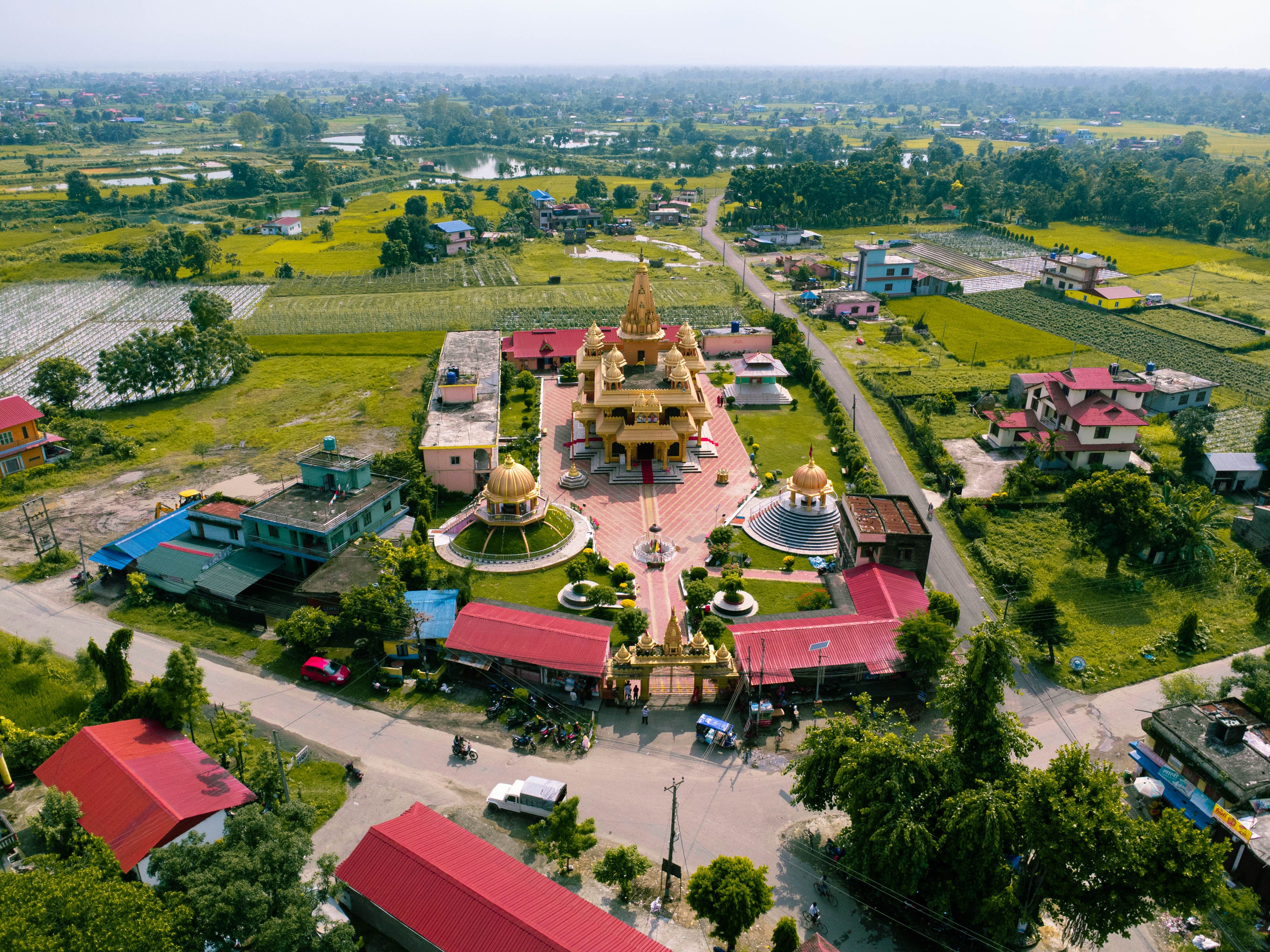 Explore an aerial panorama showing a stunning golden temple surrounded by lush fields and village houses.