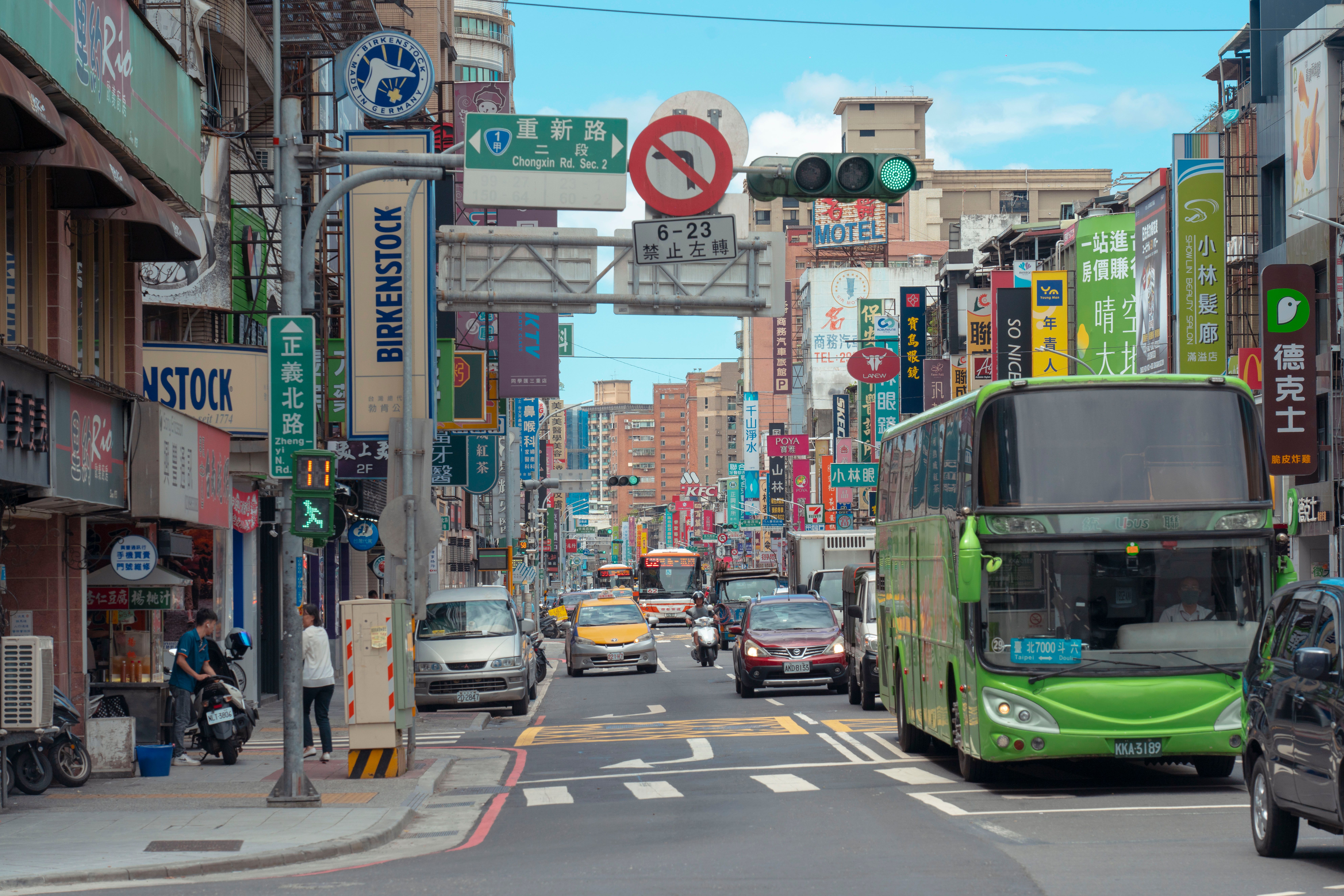 Busy urban street in Taipei with colorful signs, buses, and pedestrians under bright daylight