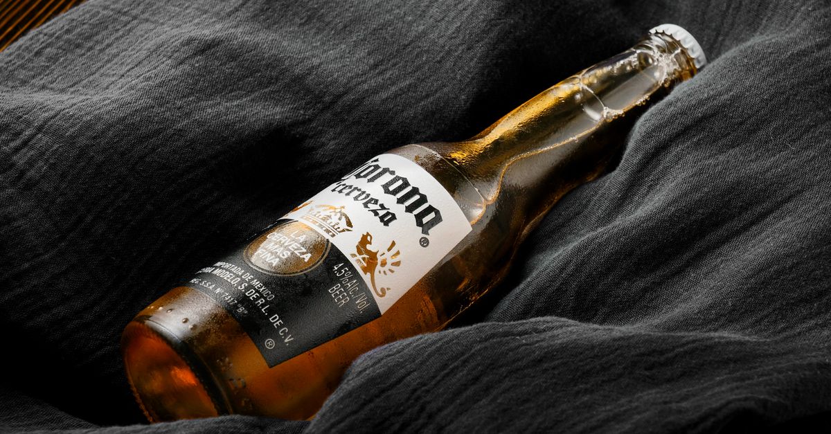 A Corona beer bottle resting on dark textured fabric, highlighting luxury and relaxation.