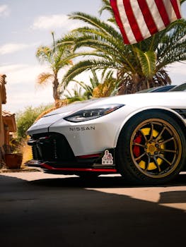 Close-up of a Nissan car with vibrant wheels under palm trees, American flag waving nearby.