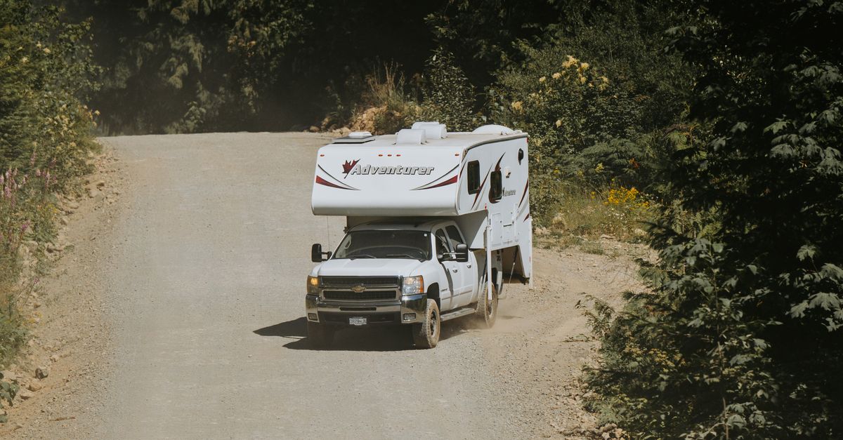 A white camper truck navigates a winding dirt road in a lush, forested area, perfect for adventure travel.