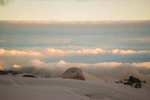 Free A peaceful camping scene atop a snow-covered mountain with clouds and sunset hues. Stock Photo