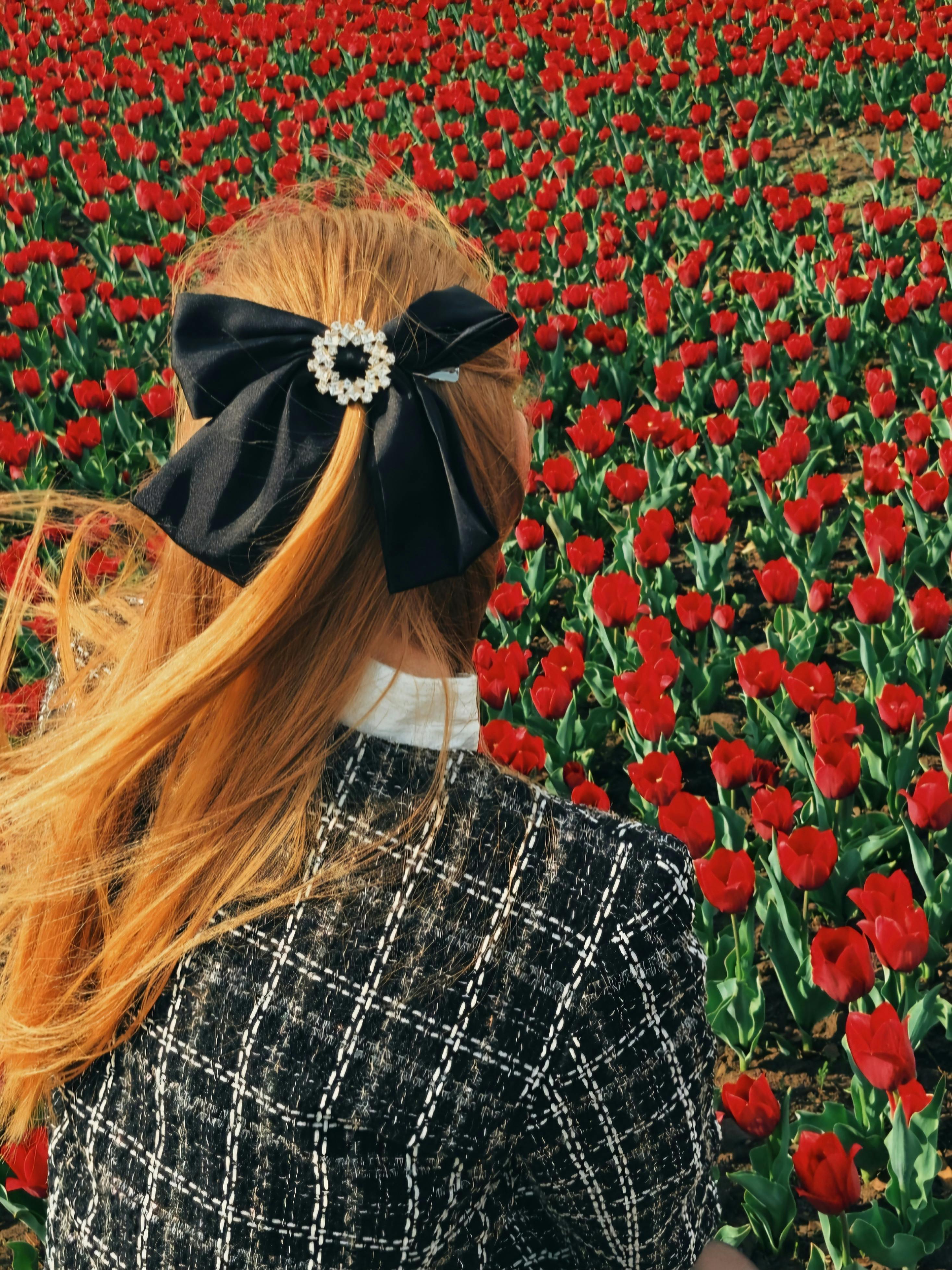 A woman with red hair and a bow accessory in a vibrant tulip field during summer.