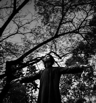 一名男子在错综复杂的树枝下摆姿势，背景的黑白对比引人注目