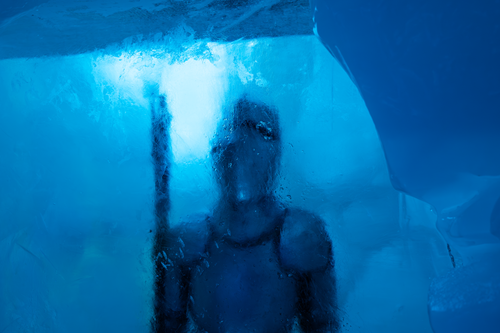 Free A mysterious figure in scuba gear behind a sheet of ice, bathed in blue light. Stock Photo