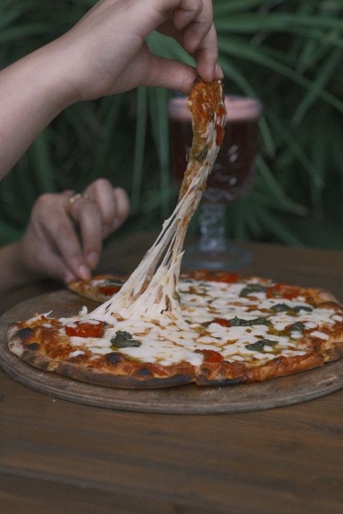 Free Close-up of a hand pulling stretchy cheese from a delicious pizza outdoors. Stock Photo