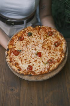 Homemade pizza topped with melted cheese and cherry tomato slices served on a wooden table.