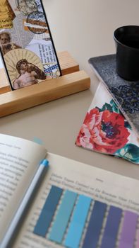 Creative workspace setup featuring an open book, colorful notebook, and tablet stand with art display.
