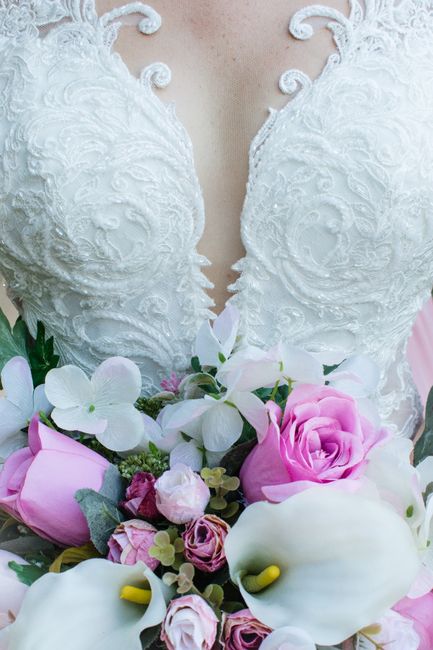 Close-up of a bride's lace wedding dress with a vibrant bouquet of pink roses and white calla lilies.