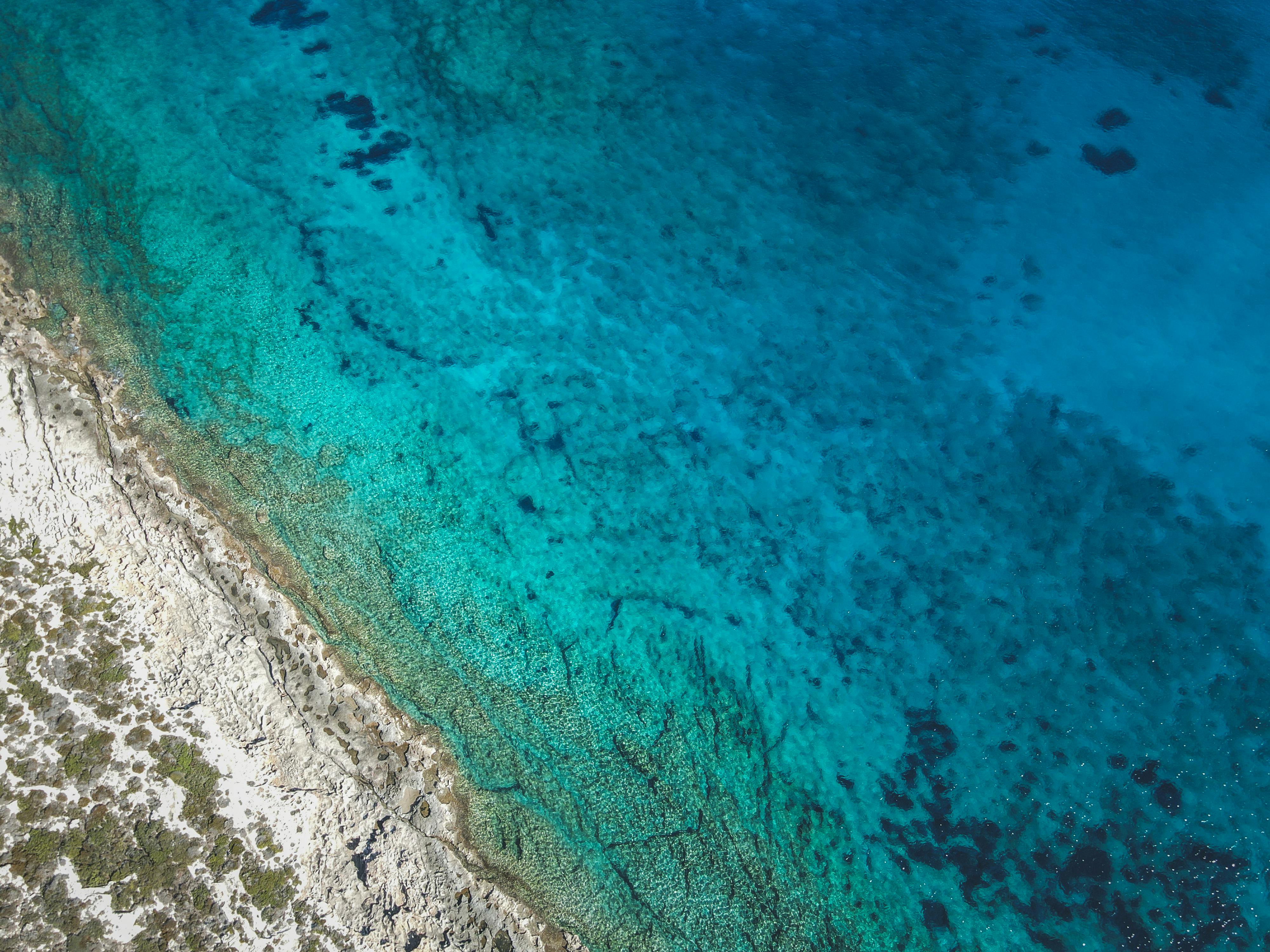 Stunning aerial view of clear turquoise ocean beside rocky coastline.
