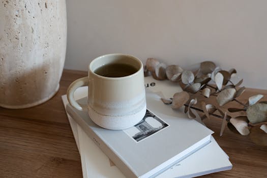 A serene still life featuring a ceramic mug of tea, dried eucalyptus, and books on a wooden table.