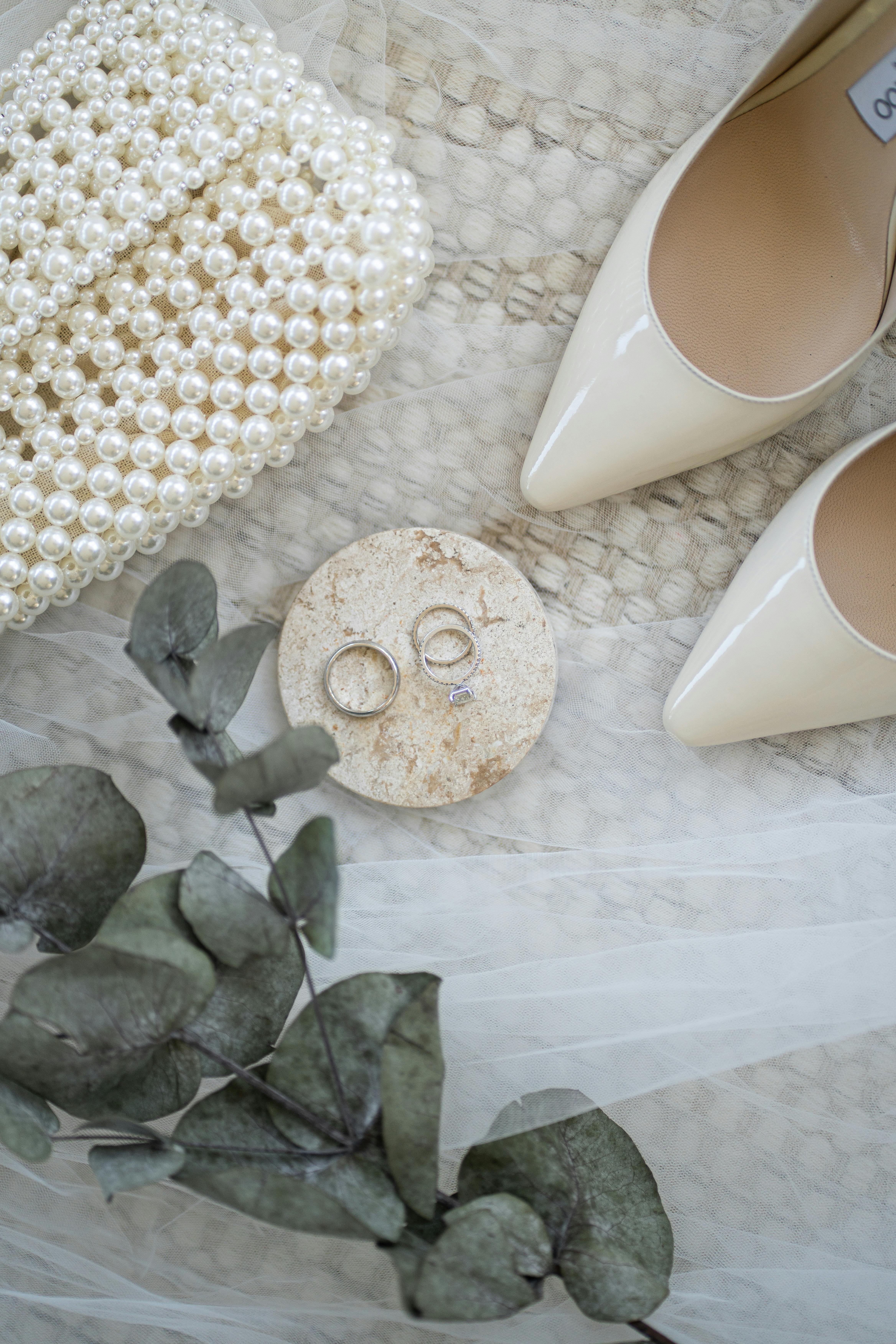 Flat lay of elegant wedding accessories including rings, pearl clutch, and high heels.