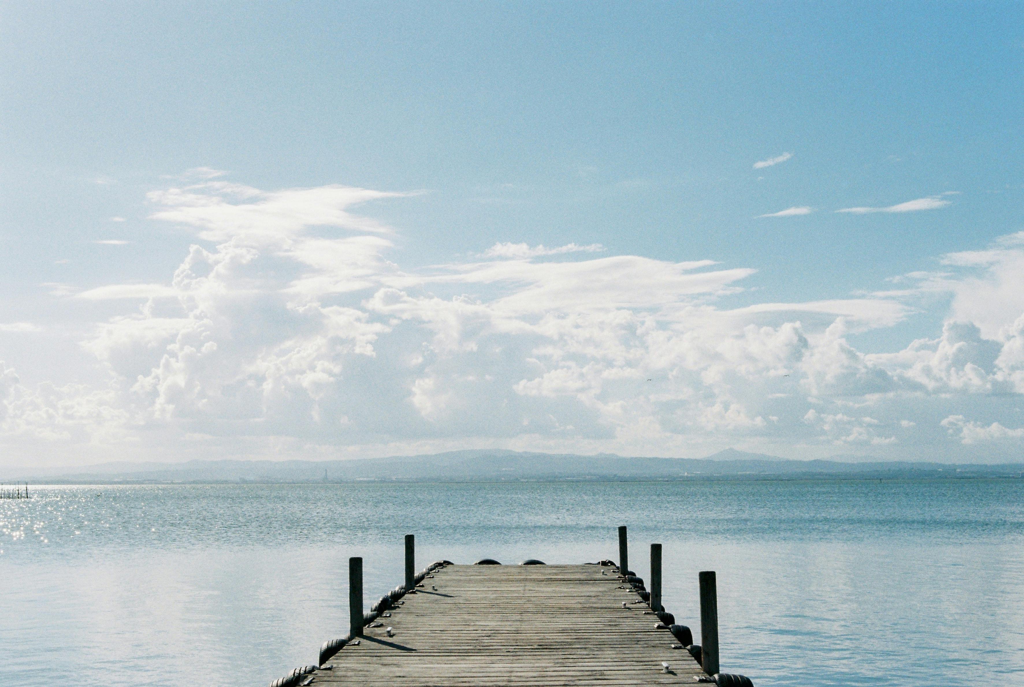 A serene view over a wooden pier stretching into a calm lake under a vast cloudy sky.