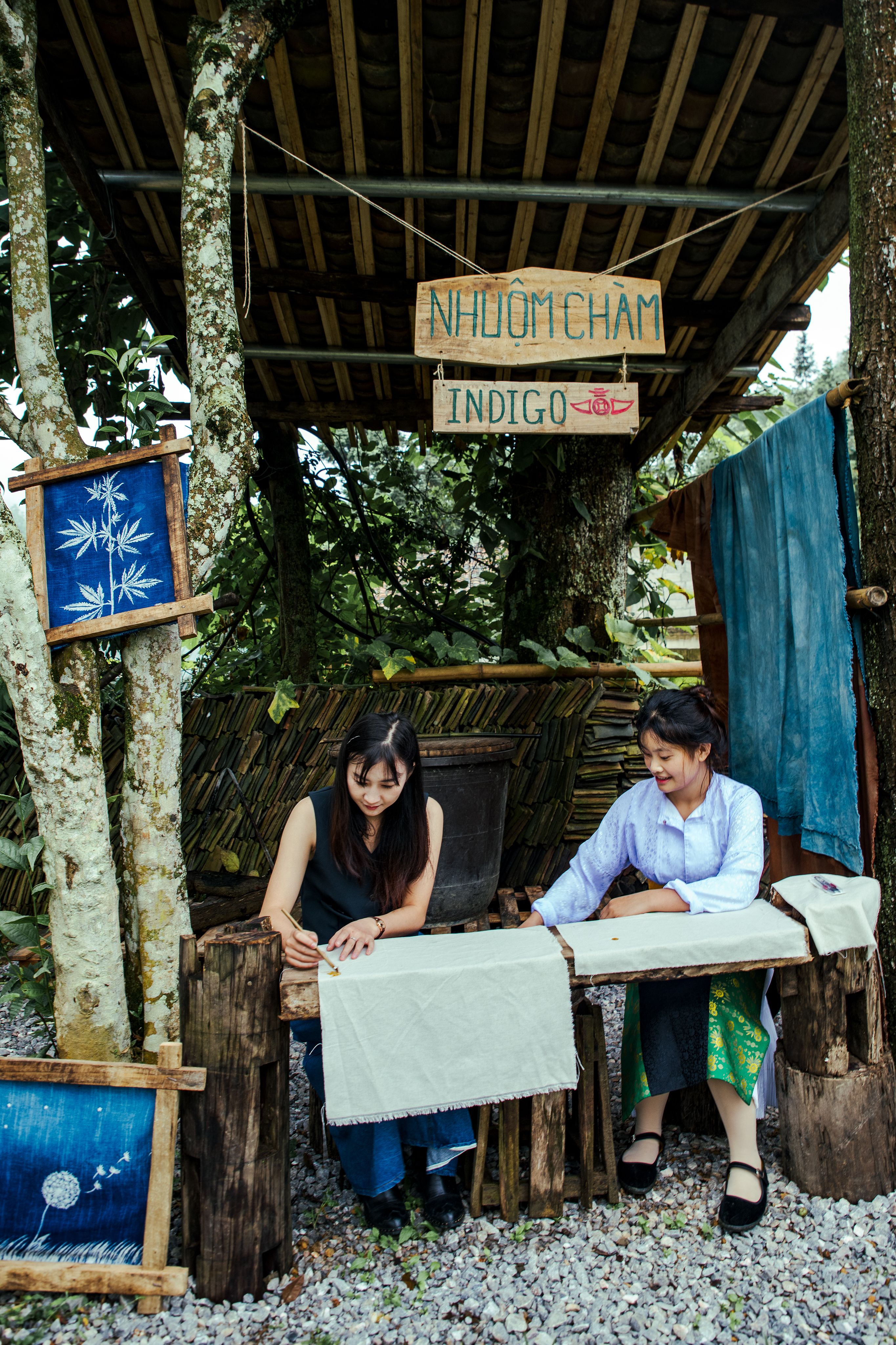 Two women engaging in indigo dyeing at a rustic outdoor setting, showcasing traditional craftsmanship.