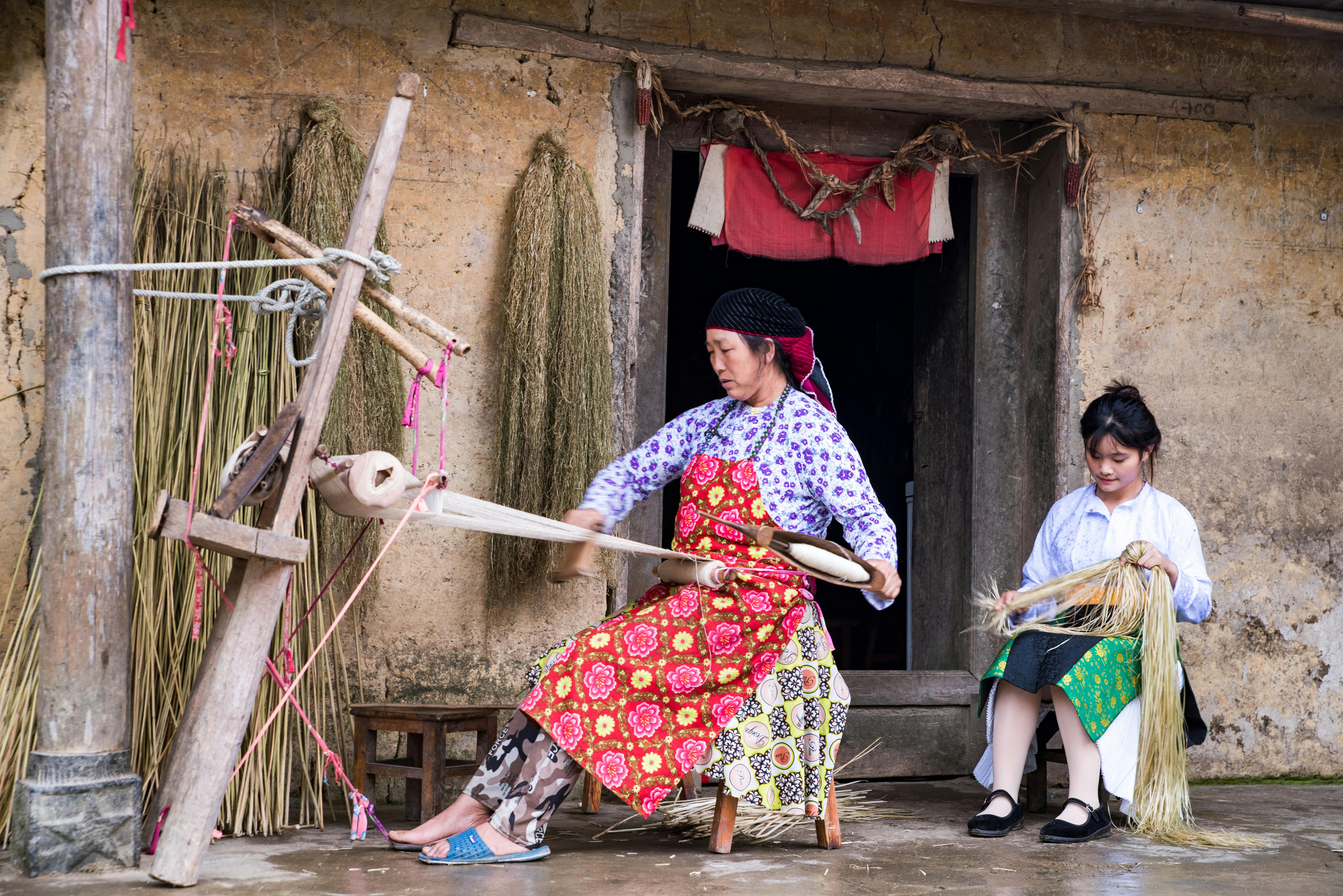 mother working on loom and daughter sitting behind