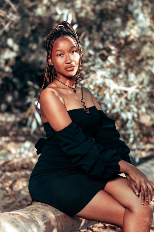 Free Portrait of a woman in black dress sitting on a log outdoors. Autumn vibes. Stock Photo