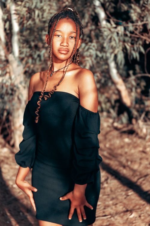 Free Chic portrait of a young woman in a stylish black dress, posing confidently outdoors with a natural background. Stock Photo