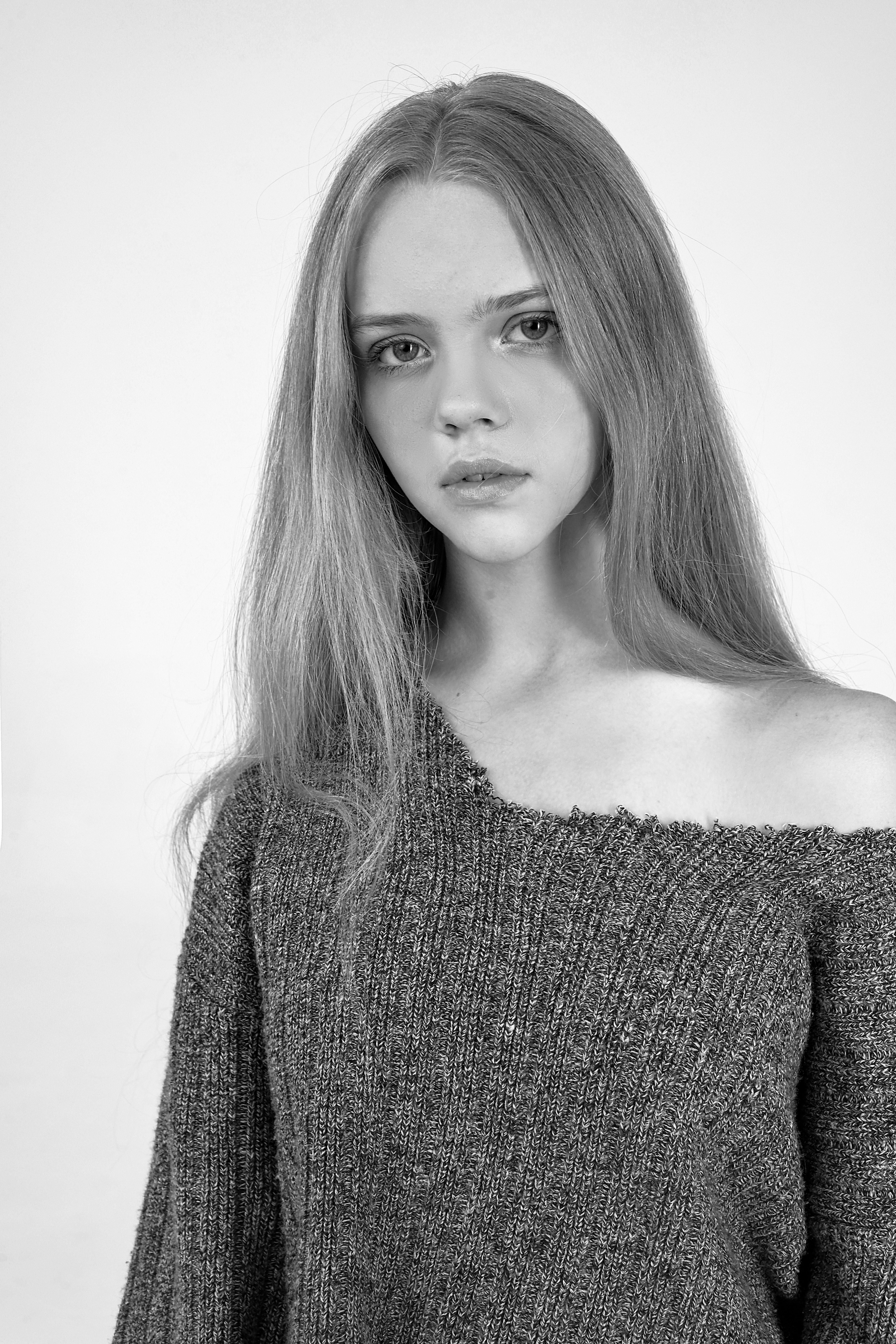 Black and white portrait of a young woman with long hair in an off-shoulder sweater.