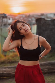 在金色的日落户外，一名年轻女子身穿黑色露脐上衣和红色裙子，时尚地摆着姿势