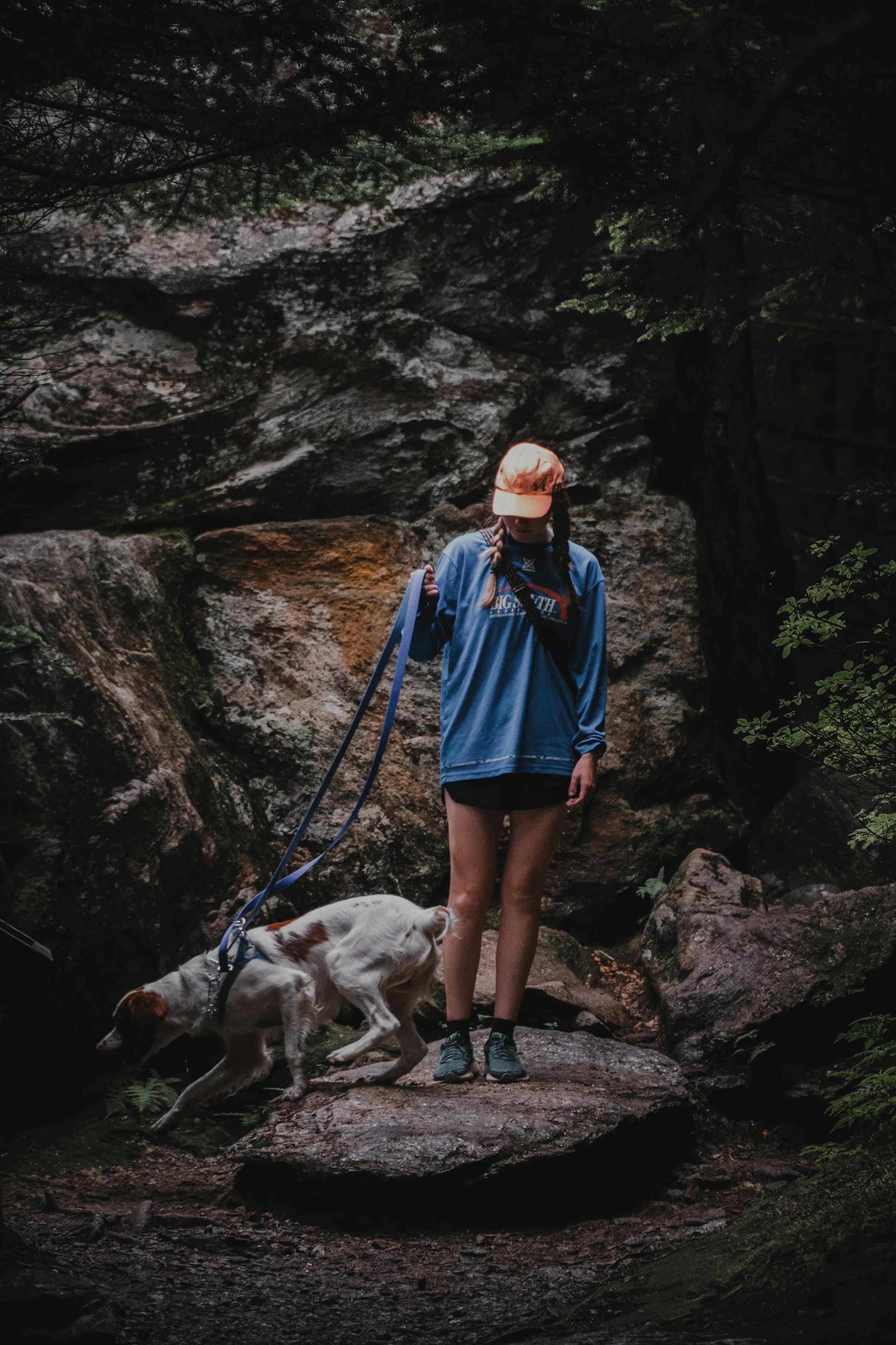 一名妇女身着户外装备，带着她的狗穿过茂密的森林，四周岩石遍布